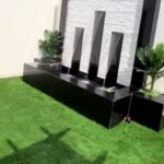 شلال مياه صناعي مع نافورة وحديقة مزينة بالنباتات وأحواض الزهور، تصميم هادئ وجذاب.