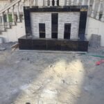 شلال صناعي مع نافورة مائية وحديقة مزينة بأحواض زهور وجلسة خارجية حديثة.