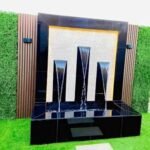 شلال صناعي مع نافورة مائية وحديقة مزينة بأحواض زهور وجلسة خارجية بتصميم عصري.